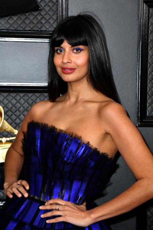 Jameela Jamil smiling wearing a strapless black and blue dress with her hands on her hips.