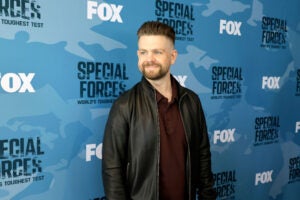 Jack Osbourne attends the red carpet for Fox's "Special Forces: World's Toughest Test" smiling facing left wearing a leather jacket.